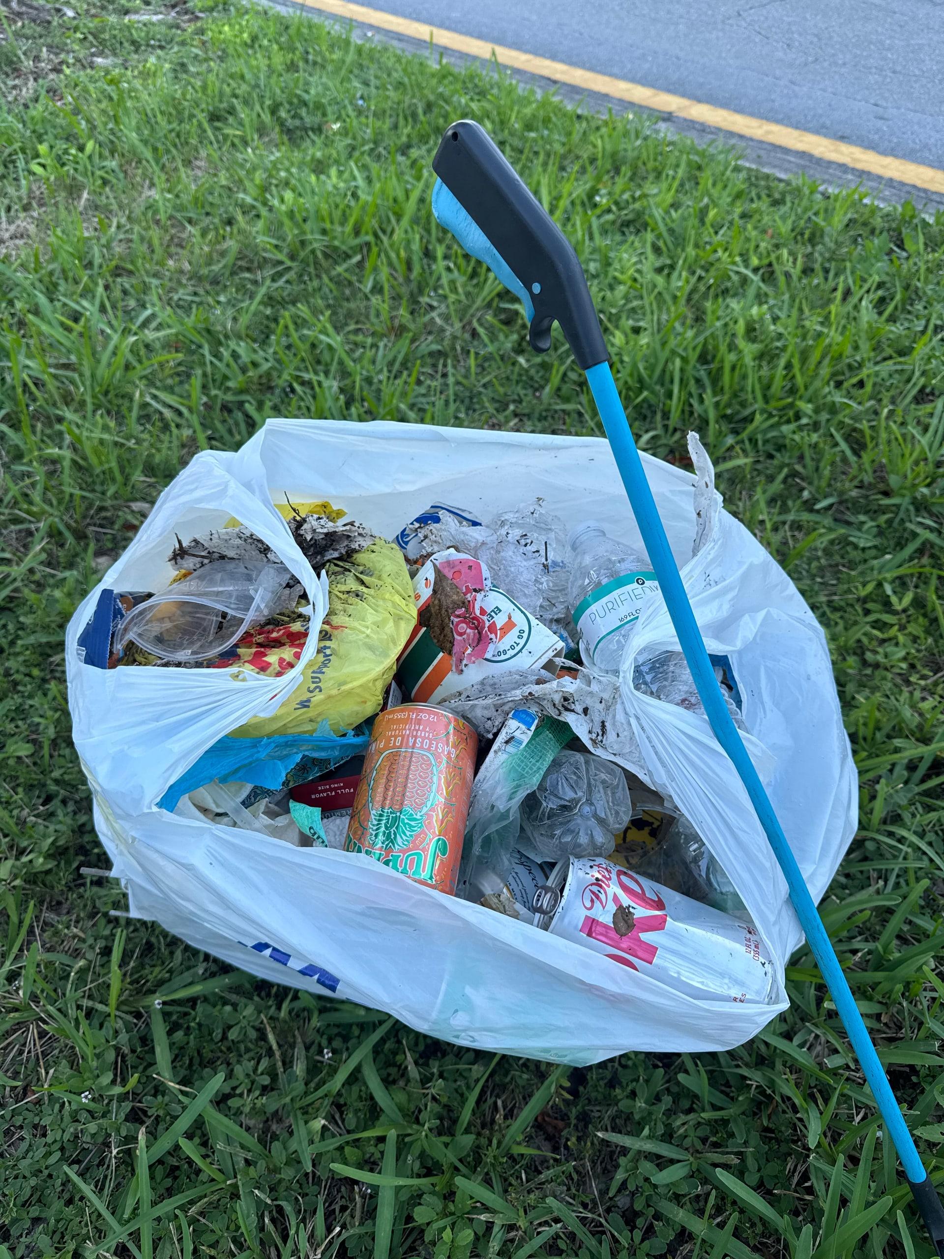 A bag of bottles and cans collected along the road with a litter grabber tool